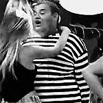 a man and a woman are hugging each other in a black and white photo . the man is wearing a striped shirt .