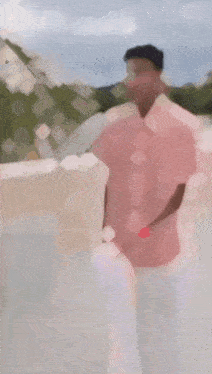 a man in a pink shirt and white dhoti is holding a white towel while walking .