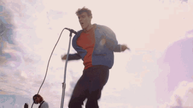 a man wearing a red shirt and a blue jacket is kicking a pole