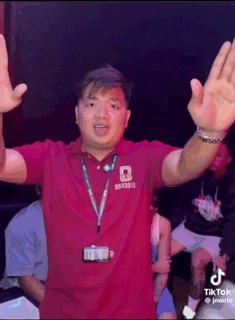 a man in a red shirt is standing with his arms outstretched in a dark room .