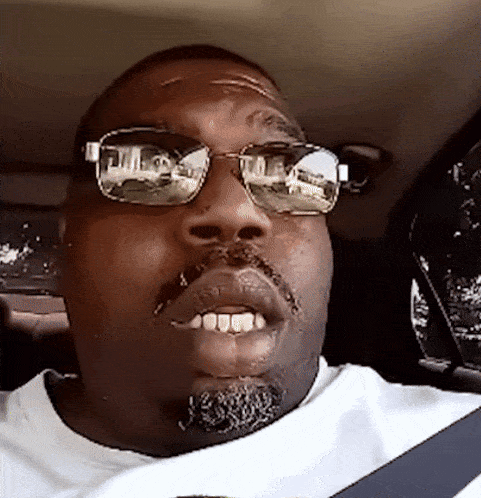 a man wearing sunglasses and a white shirt is driving a car
