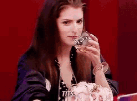 a woman is sitting at a table holding a glass of wine and a bouquet of flowers .