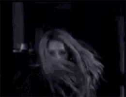 a woman with long blonde hair and a black eye is standing in the dark .