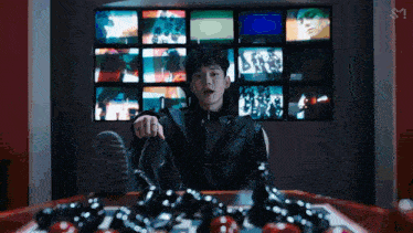 a young man is sitting at a table with a chess board in front of a wall of televisions .