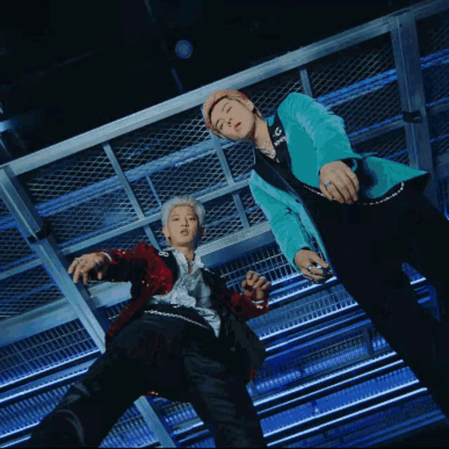 two men standing next to each other with one wearing a red jacket