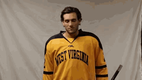 a man wearing a yellow west virginia jersey holds a hockey stick
