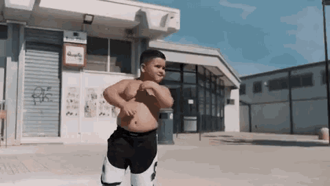 a boy without a shirt is standing in front of a building .