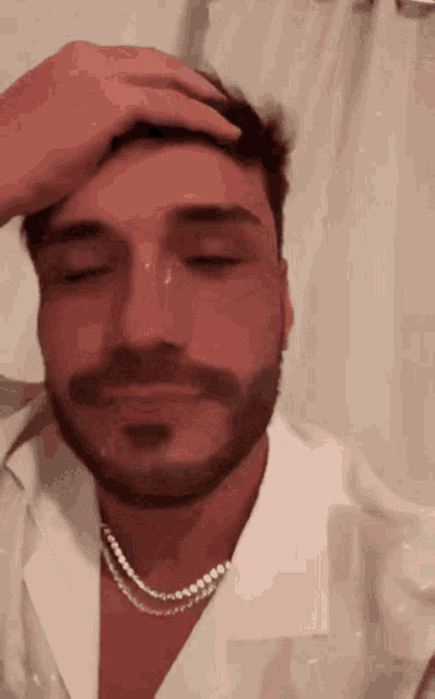 a man with a beard and a pearl necklace is holding his hand to his head .