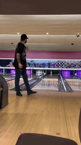 a man in a black shirt is bowling on a pink and purple bowling alley