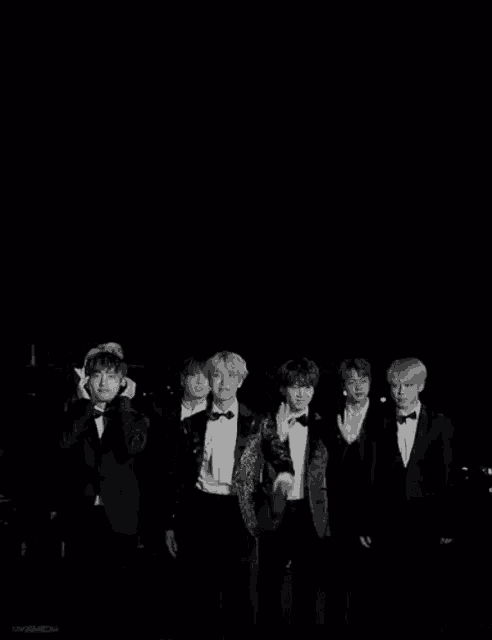 a black and white photo of a group of young men in tuxedos standing next to each other .