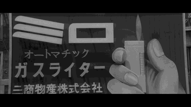 a black and white photo of a hand holding a lighter with foreign writing