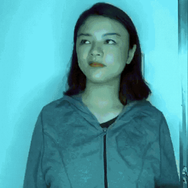 a woman wearing a grey hoodie is looking at the camera