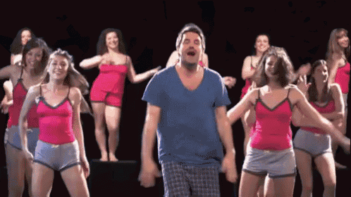 a group of women are dancing with a man in a blue shirt in the middle