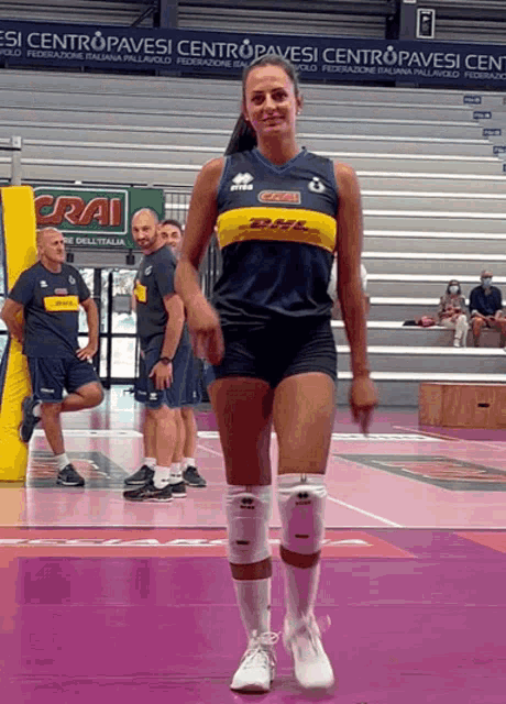 a woman in a dhl shirt is walking on a purple court