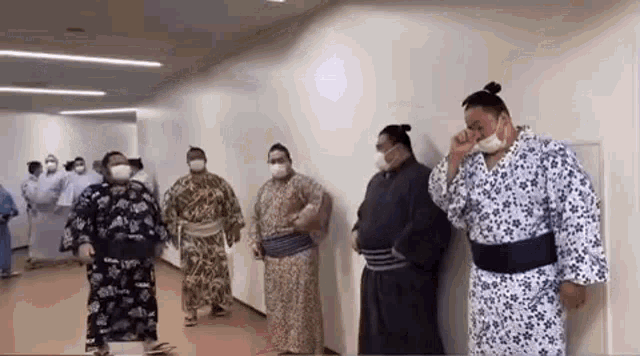 a group of sumo wrestlers wearing masks are standing in a hallway .
