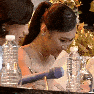 a woman sits at a table with a microphone and bottles of water