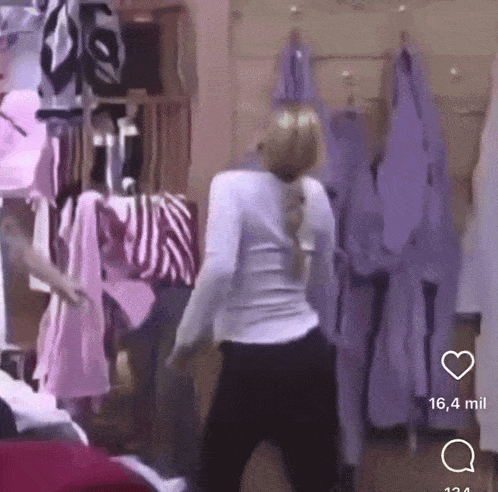 a woman is dancing in a room with purple clothes hanging on a rack