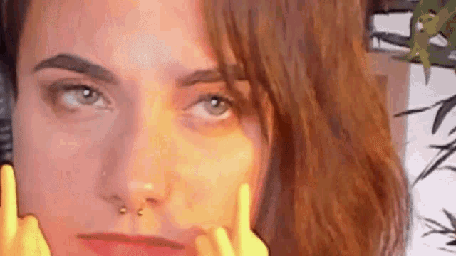 a close up of a woman 's face with a nose ring and a yellow finger .
