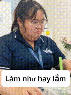 a woman wearing glasses is sitting at a table with a sign that says lam như hay lam in front of her