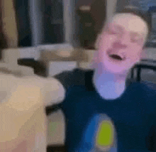 a man in a blue shirt is laughing with his eyes closed in a living room .