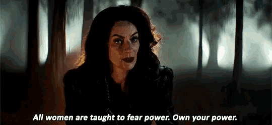 a woman in a black jacket is standing in a dark room and talking .