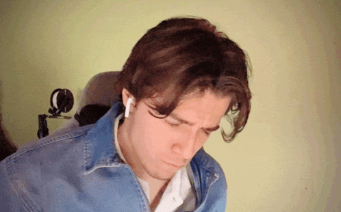 a man wearing a denim jacket and ear buds looks down