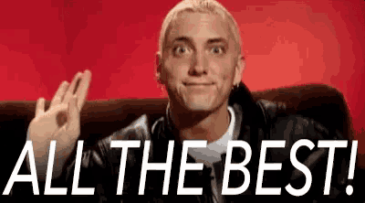 a man is sitting on a couch giving an ok sign and the words `` all the best '' behind him .