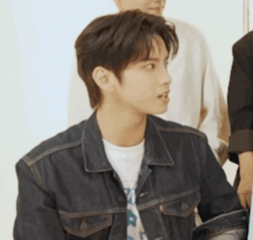 a young man wearing a denim jacket and a white t-shirt looks to the side .