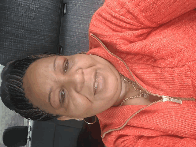 a woman wearing a red sweater and earrings smiles in a car