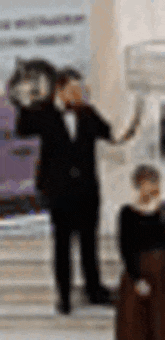 a man in a tuxedo is standing next to a woman in a black dress holding a clock .