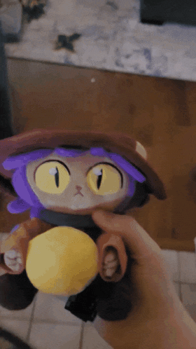 a person holding a stuffed animal with yellow eyes and purple hair