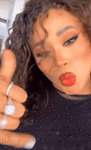 a woman with curly hair is giving a thumbs up sign