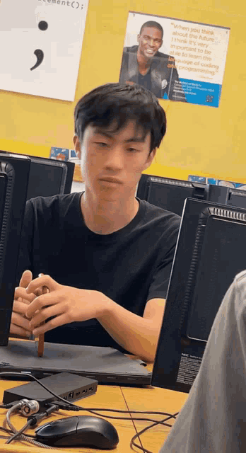 a man is sitting in front of a computer with a poster on the wall that says " you never think about the future "