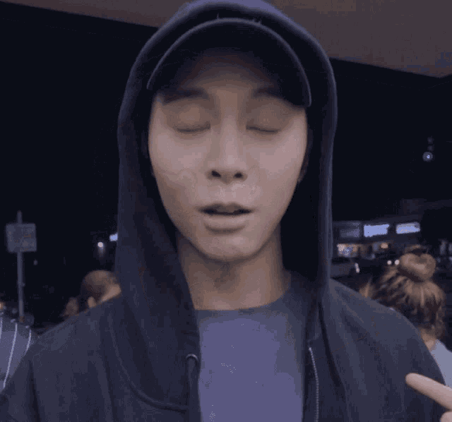 a man with his eyes closed wearing a black hoodie and hat