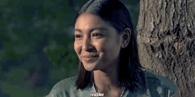a woman in a camouflage shirt is smiling in front of a tree