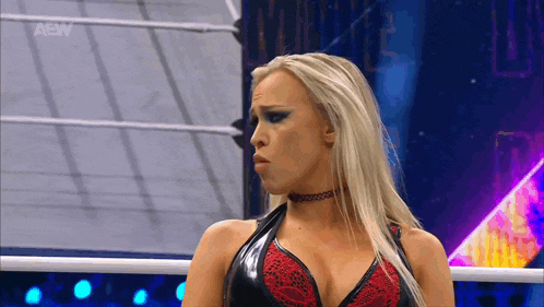 a woman is standing in a wrestling ring wearing a choker and a black and red top .