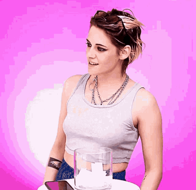 a woman in a tank top stands next to a glass on a pink background