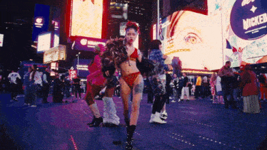 a woman in a bikini stands in front of a billboard that says miracle