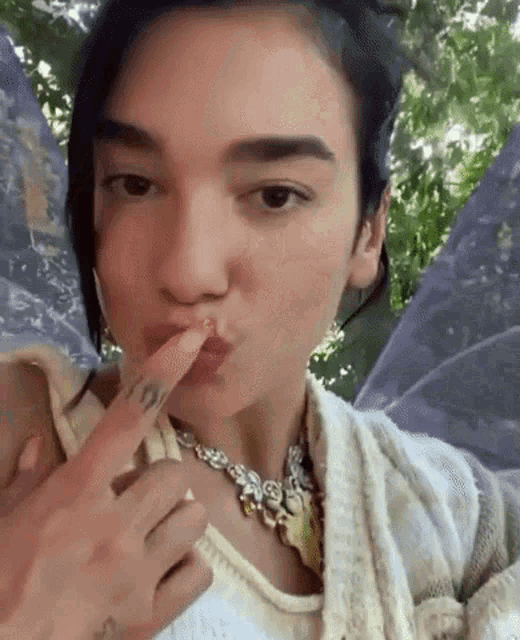 a woman with fairy wings on her shoulder is taking a selfie with her finger to her mouth .