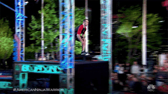 a man in a red shirt is jumping over a box on a nbc show