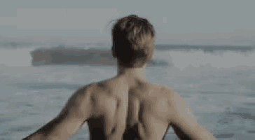 a shirtless man is standing on a beach looking at the ocean .