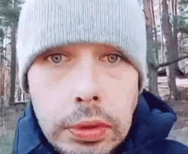 a man with a beard wearing a beanie and a blue jacket is looking at the camera .