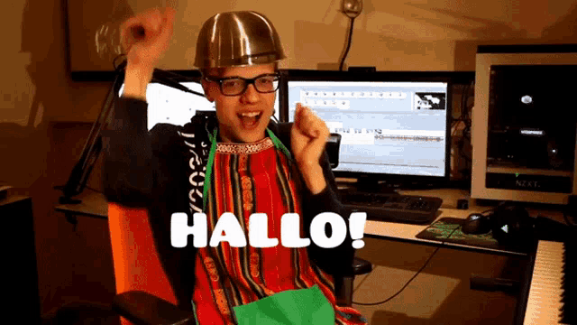 a man wearing an apron and a hard hat says hallo in front of a computer