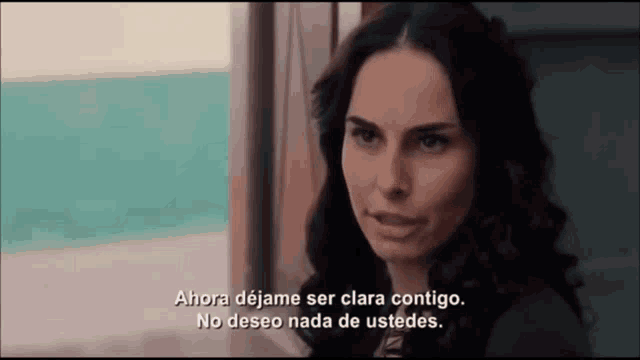 a woman is looking out a window with a caption that says " ahora dejame ser clara contigo "
