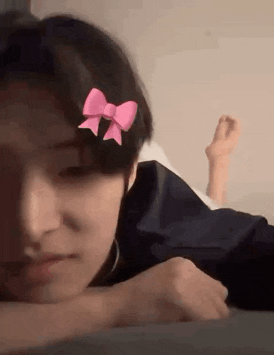 a person is laying on a bed with their feet up and a pink bow in their hair .
