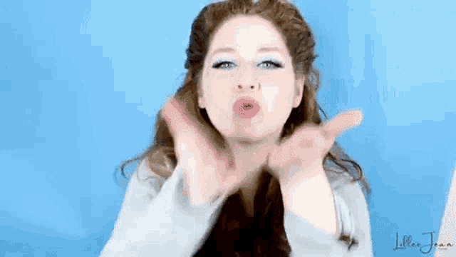 a woman is blowing a kiss with her hands in front of her face .
