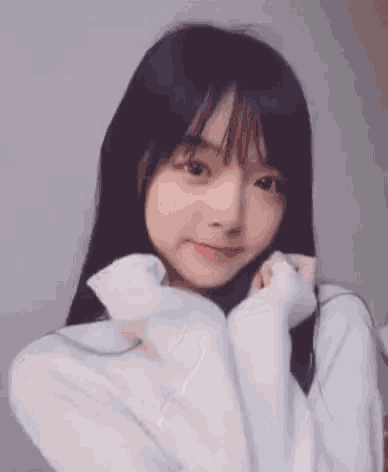 a young girl with long black hair is wearing a white sweater and making a funny face .