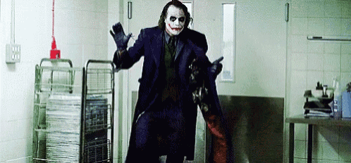 a man in a joker costume is standing in a hallway with a gun .