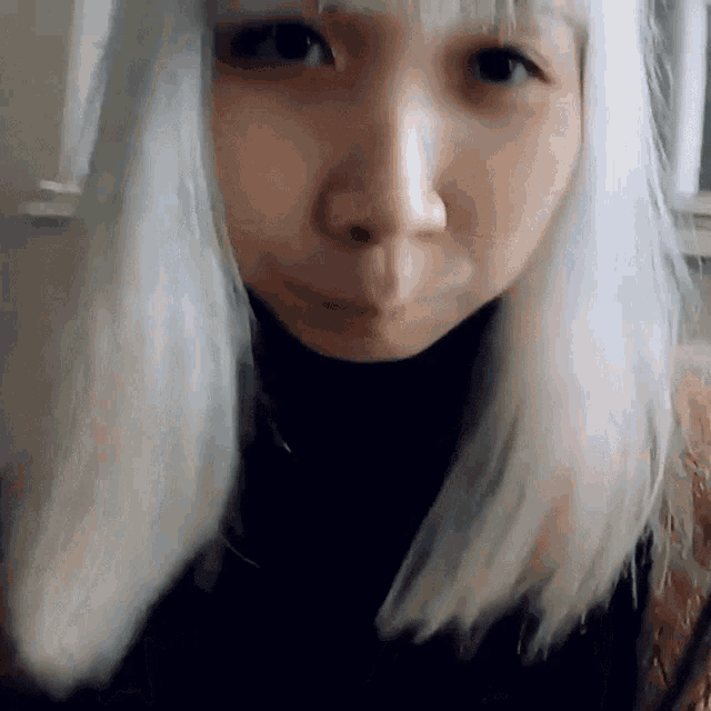 a woman with white hair and a black turtleneck looks at the camera