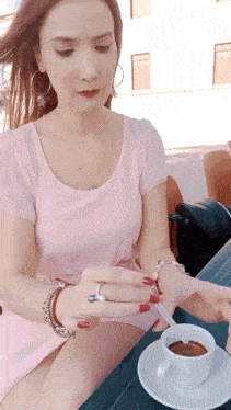 a woman in a pink shirt is sitting at a table with a cup of coffee